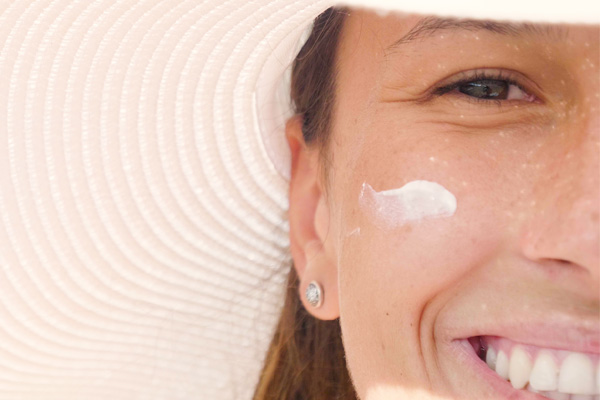 Lächelnde Frau mit breitem Sonnenhut und Sonnencreme im Gesicht